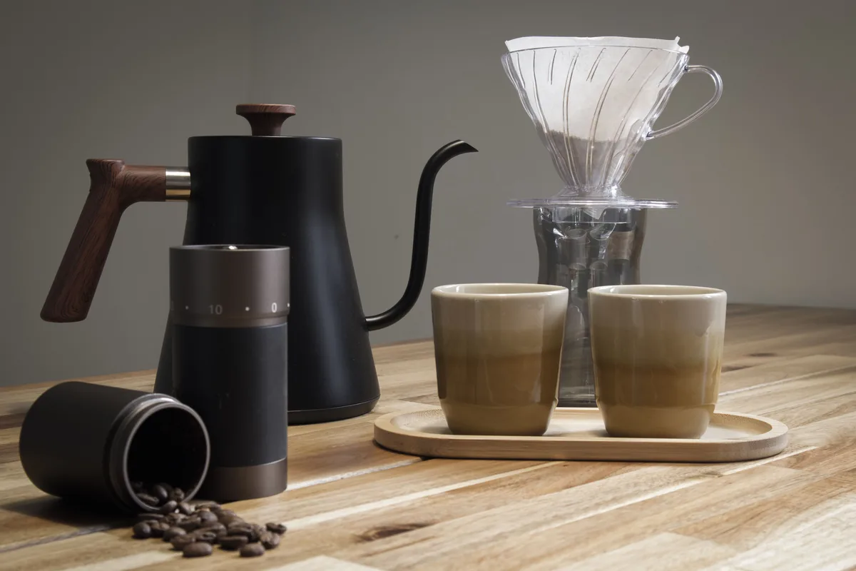 How to Brew V60 Coffee Step by Step 1 V60 dripper, gooseneck kettle, hand grinder and two cups on a wooden table